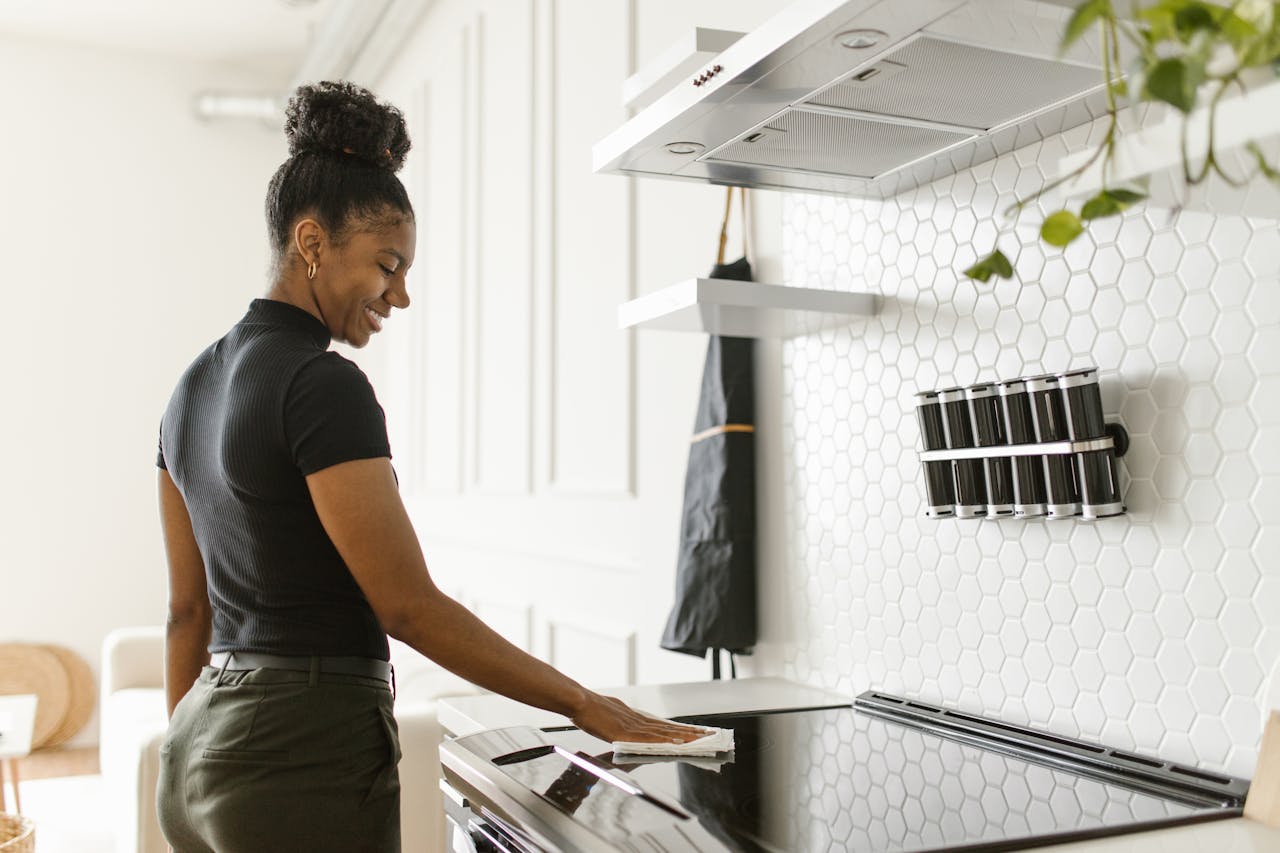 A woman cheerfully cleans her kitchen, focusing on the electric stove in a bright, modern space.